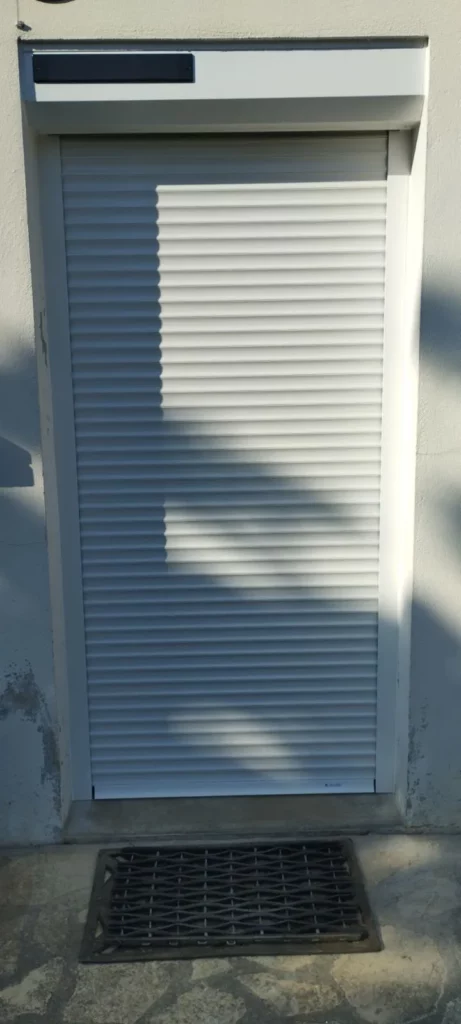 Volet roulant solaire motorisé blanc fermé sur porte d'entrée, installation sans fil à Bergerac.